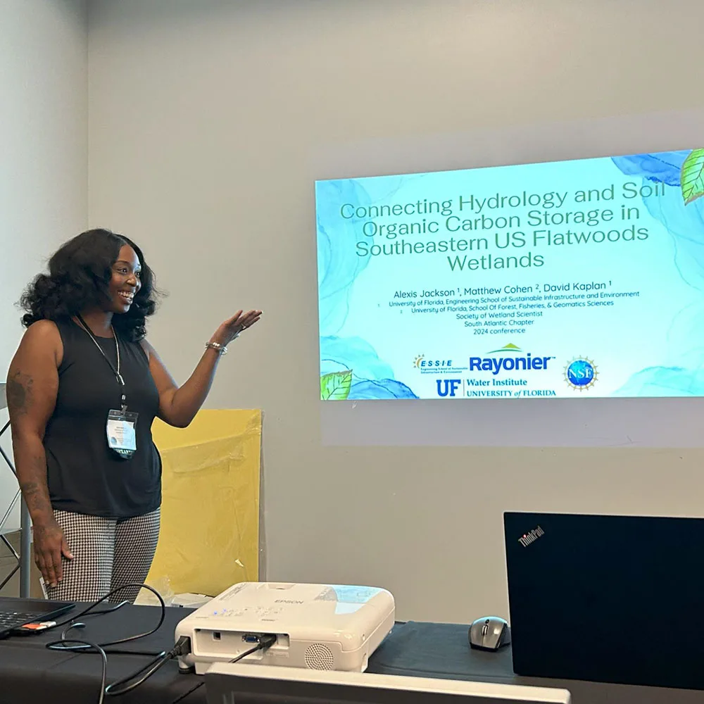 Jackson gestures toward a projected slide about hydrology and carbon storage in southeastern U.S. wetlands during a presentation.